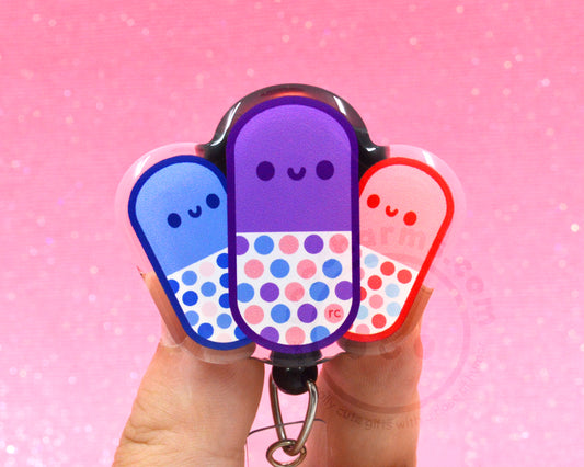 A person's hands holding a keychain with three colorful pill-shaped charms against a pink background.