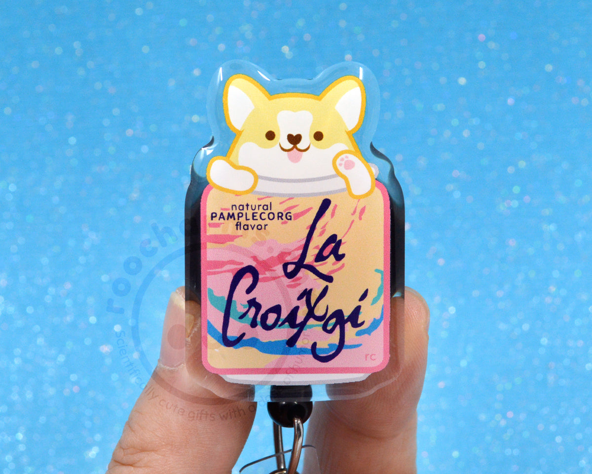 A person's hand holding a keychain with a label that features a cartoon image of a dog and text that says "La Croxigi" in a pink and yellow color scheme.