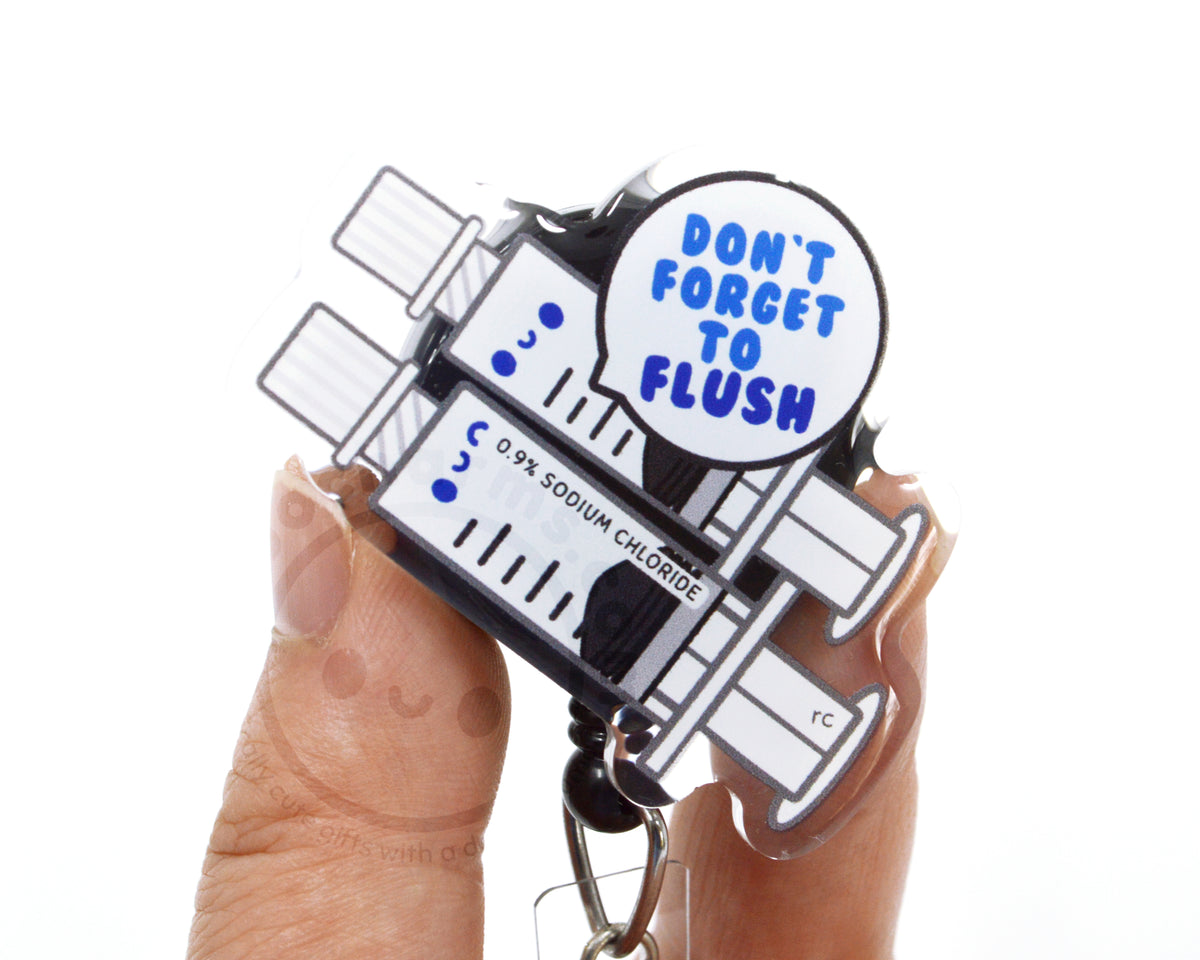 a person's hands holding a keychain with a cartoon-style design. The keychain has a message about flushing, and it is made of clear plastic.