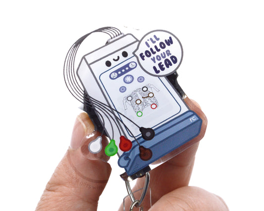 A person's hand holding a clear keychain with a cartoon-like design and text.