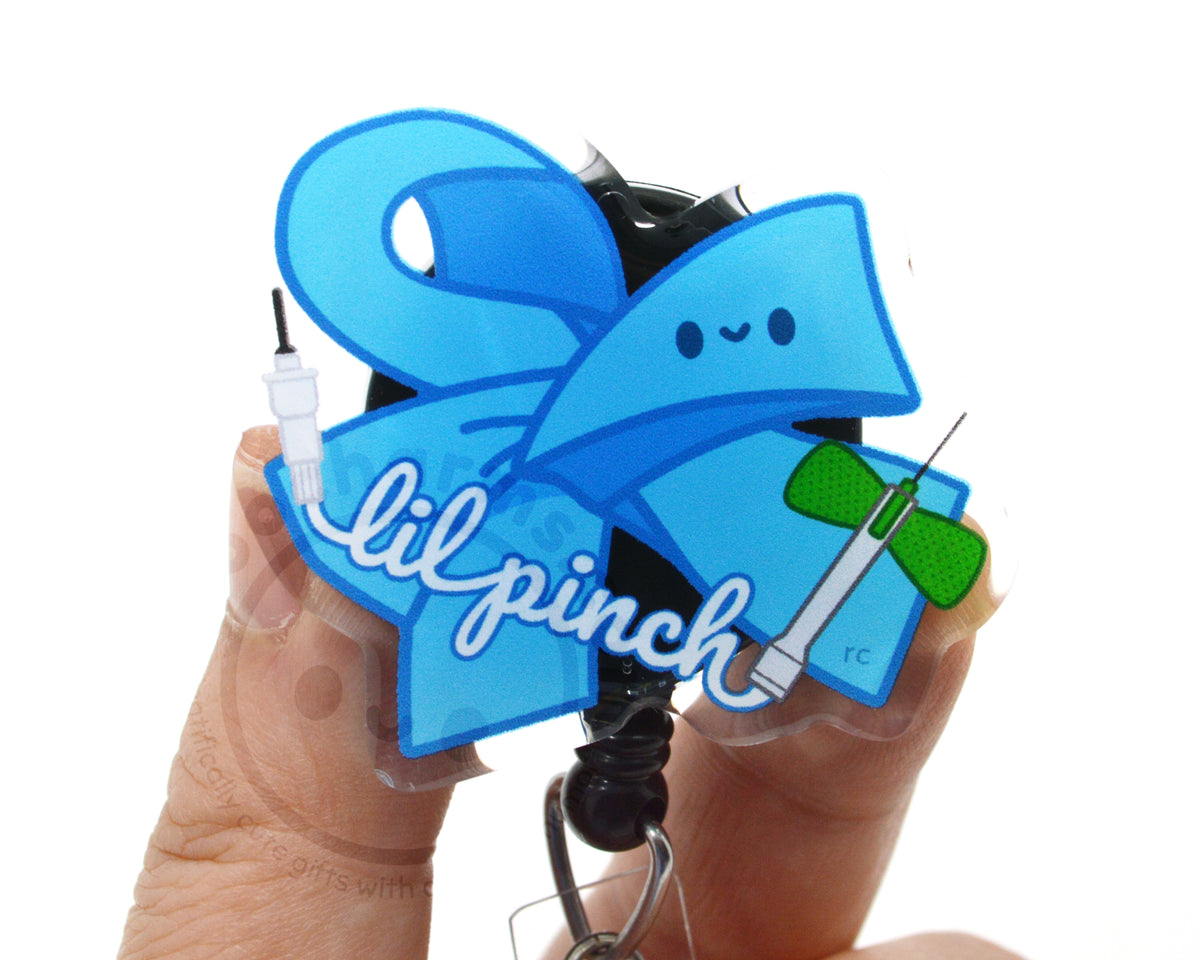 A person's hands holding a clear keychain with a blue ribbon and a green bow, along with the text "lilpinch" written on it.