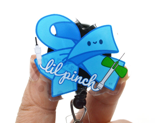 A person's hands holding a clear keychain with a blue ribbon and a green bow, along with the text "lilpinch" written on it.