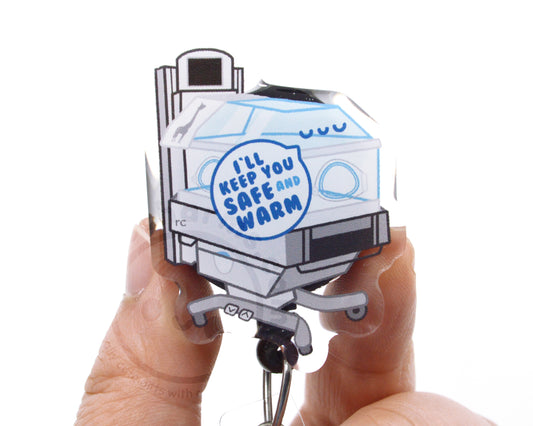 A person's hands holding a clear plastic keychain with a cartoon image of a baby crib and a message that says "I'll keep you safe and warm".