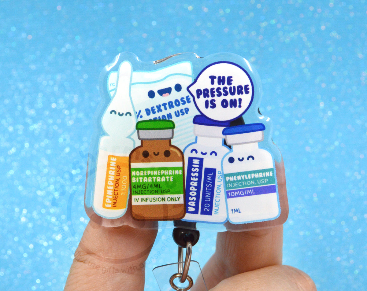 A person's fingers holding a keychain with a colorful illustration of medical bottles and a speech bubble saying "The pressure is on!".