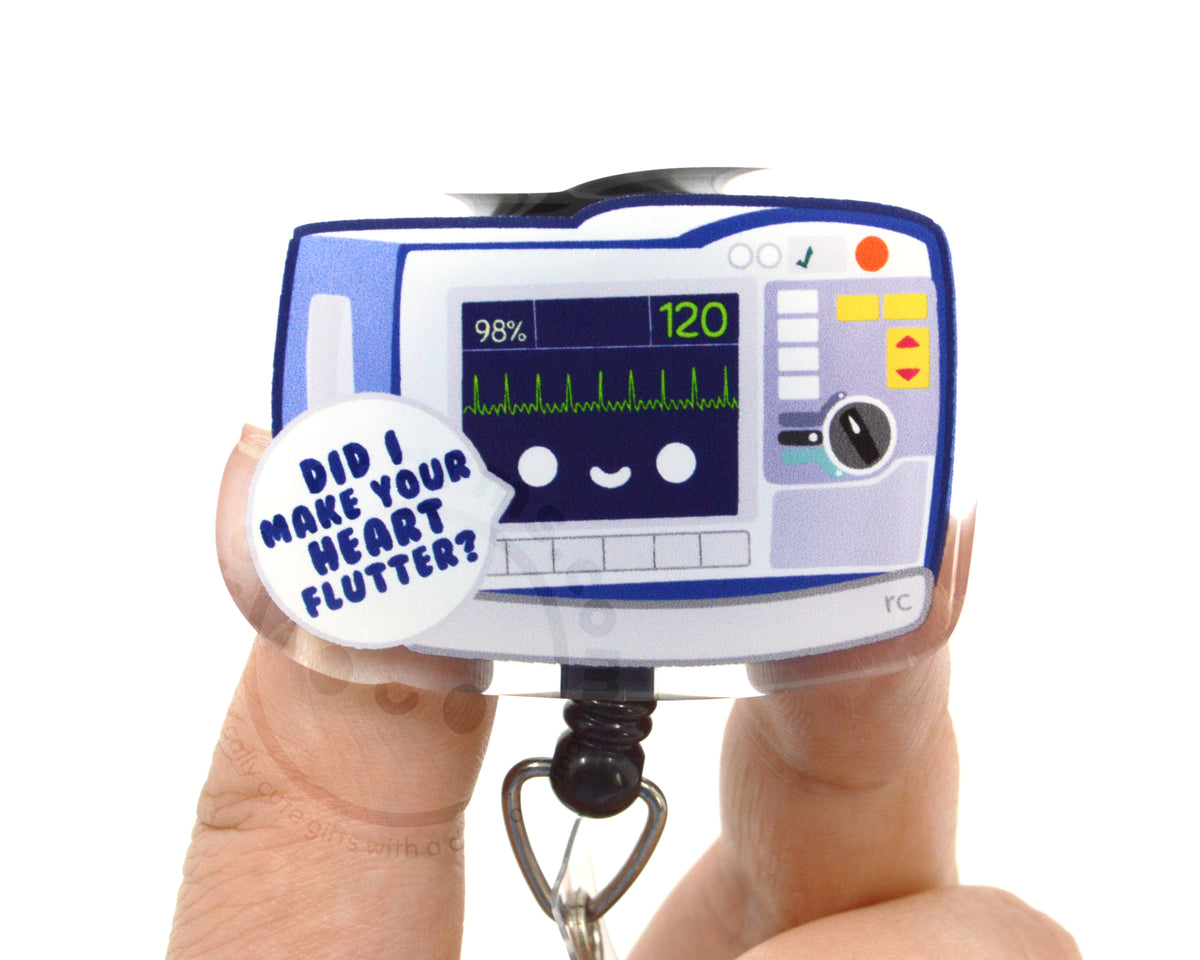 A person's fingers holding a keychain with a cartoon image of a heart monitor and a speech bubble asking "Did I make your heart flutter?".