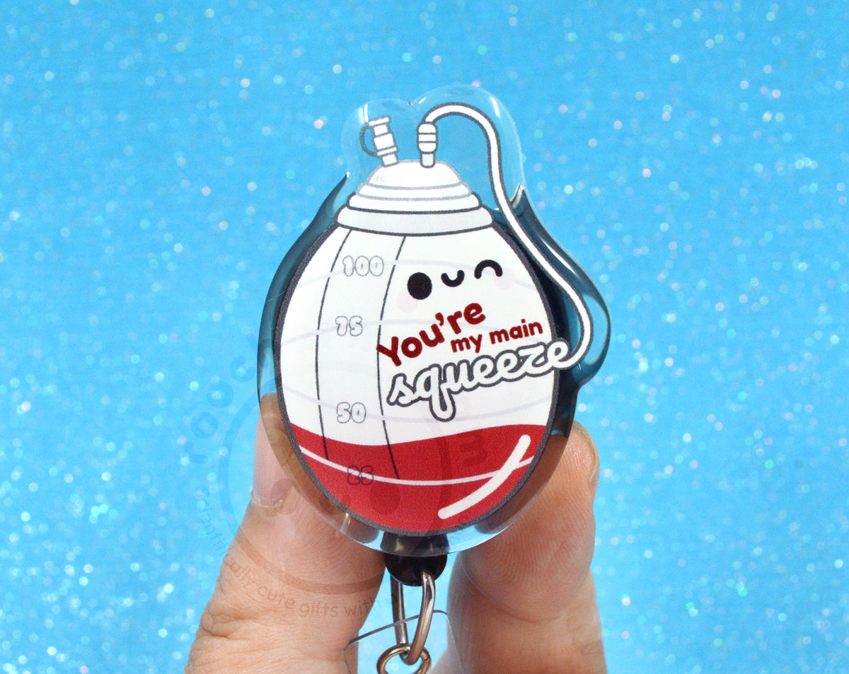 A person's hand holding a clear keychain with a cartoon image of a red and white container with a face and the text "You're my main squeeze" printed on it.