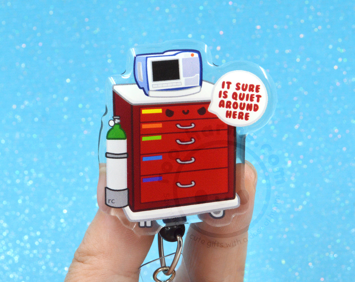 A person's hands holding a keychain with a cartoon image of a red cabinet with a computer monitor on top, and a text bubble that says "IT SURE IS QUIET AROUND HERE".